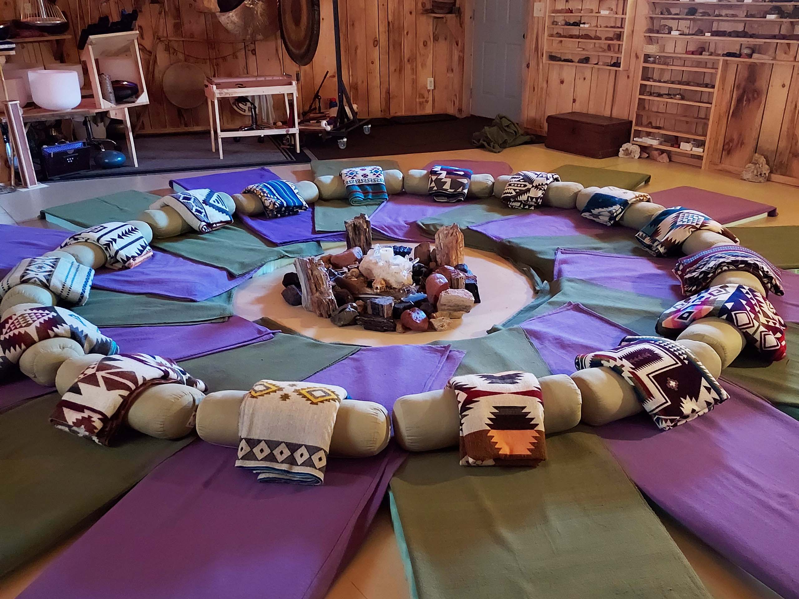 A peaceful circle of floor mats with blankets surrounded by sound meditation instruments and crystals