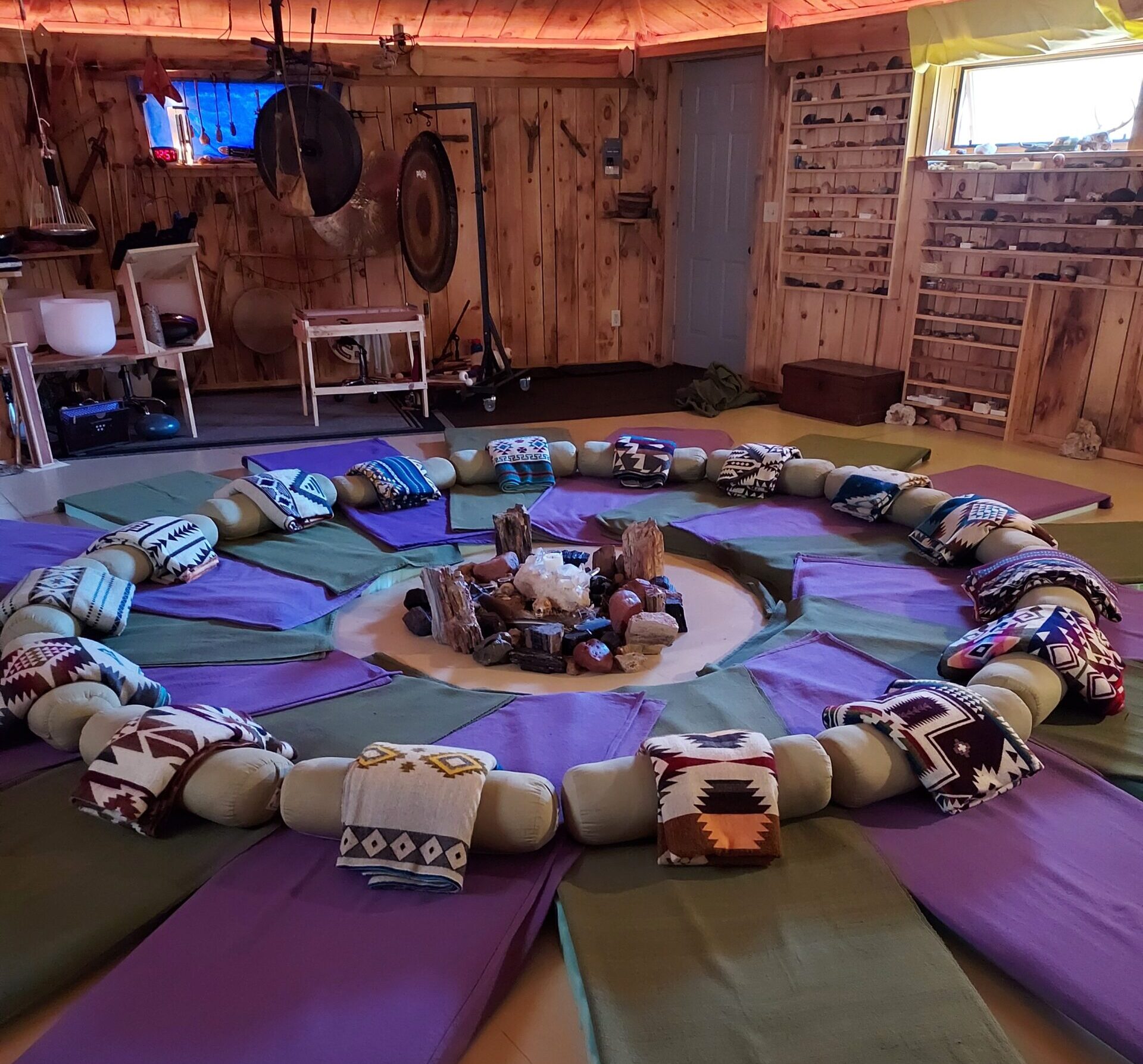 A peaceful circle of floor mats with blankets surrounded by sound meditation instruments and crystals
